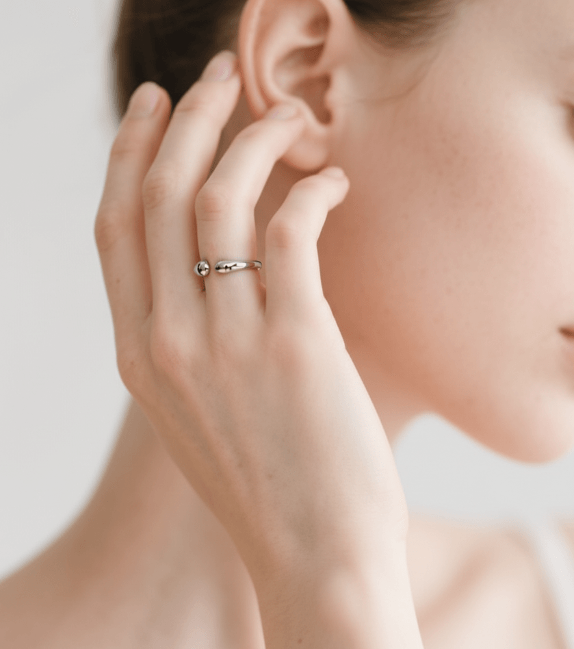 Close-up of a hand wearing a silver ring, touching the ear against a neutral background