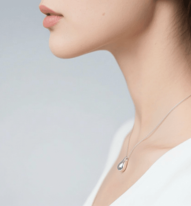 Close-up of a person wearing a silver necklace with a pendant against a light background