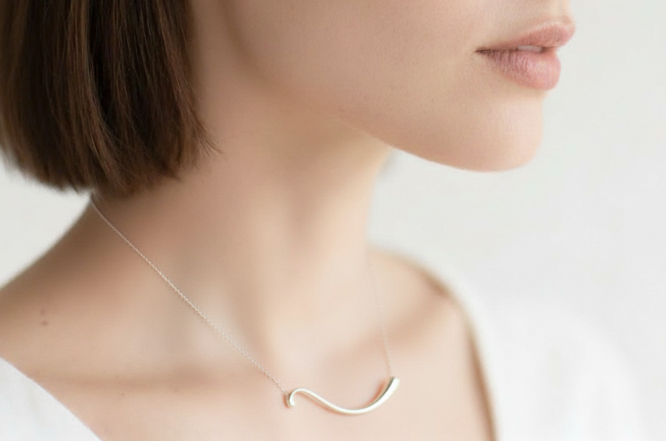 Woman wearing a delicate silver necklace against a plain background