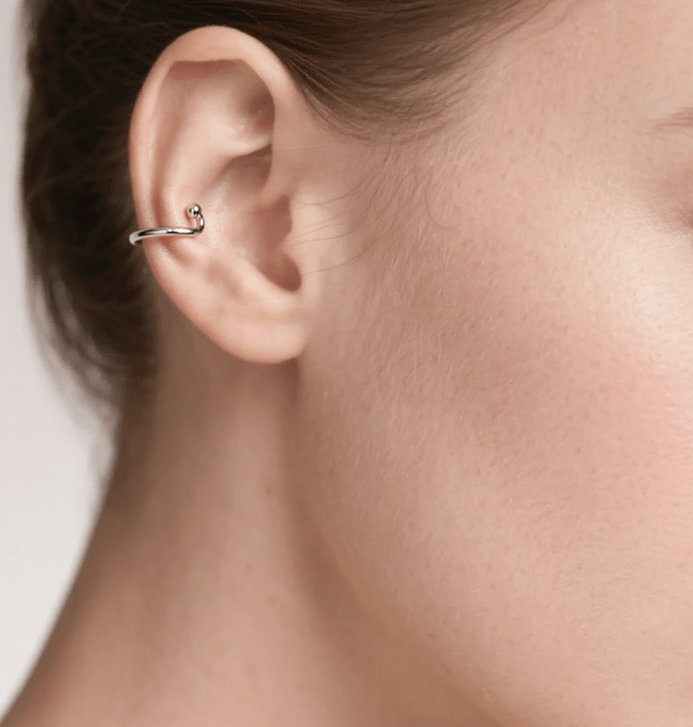 Close-up of a woman's ear wearing a silver earring with a white background